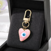 Gold heart keychain featuring a pink and white Turkish evil eye design displayed in a black velvet box.