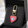 Gold heart keychain with a red evil eye charm displayed in a black velvet box.