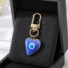 A gold-colored heart keychain featuring a blue and white evil eye design displayed in a black velvet box.
