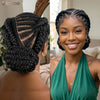 A woman shows off a short cornrow braided wig styled in an updo, featuring dark hair and gold jewelry.