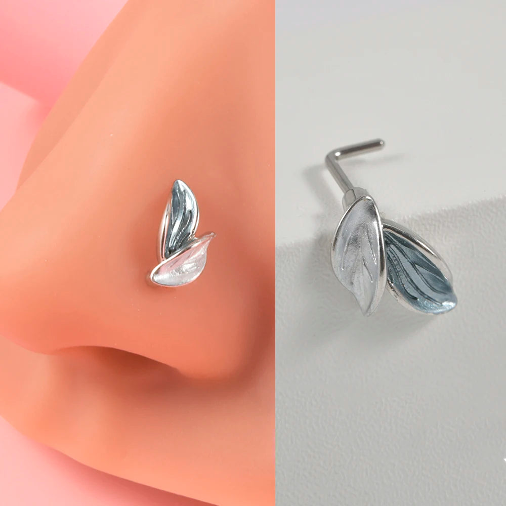Silver surgical steel demon angel nose studs shown against a peach-colored skin surface.