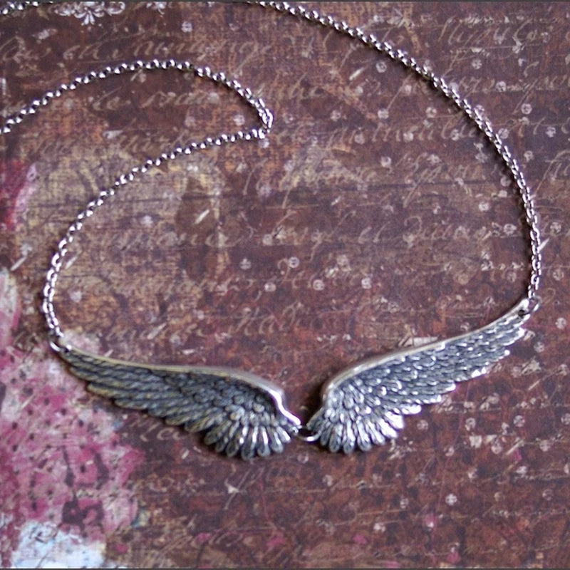 A silver feather choker necklace featuring detailed angel wings against a dark, textured background.