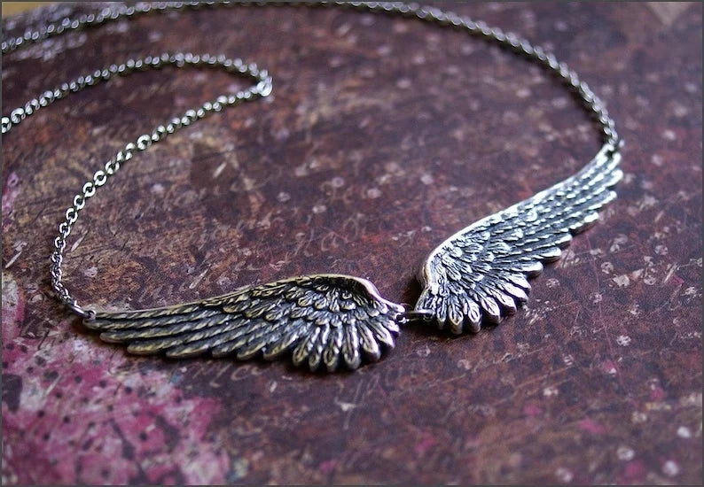 Silver feather angel wings choker necklace resting on a dark brown textured surface.