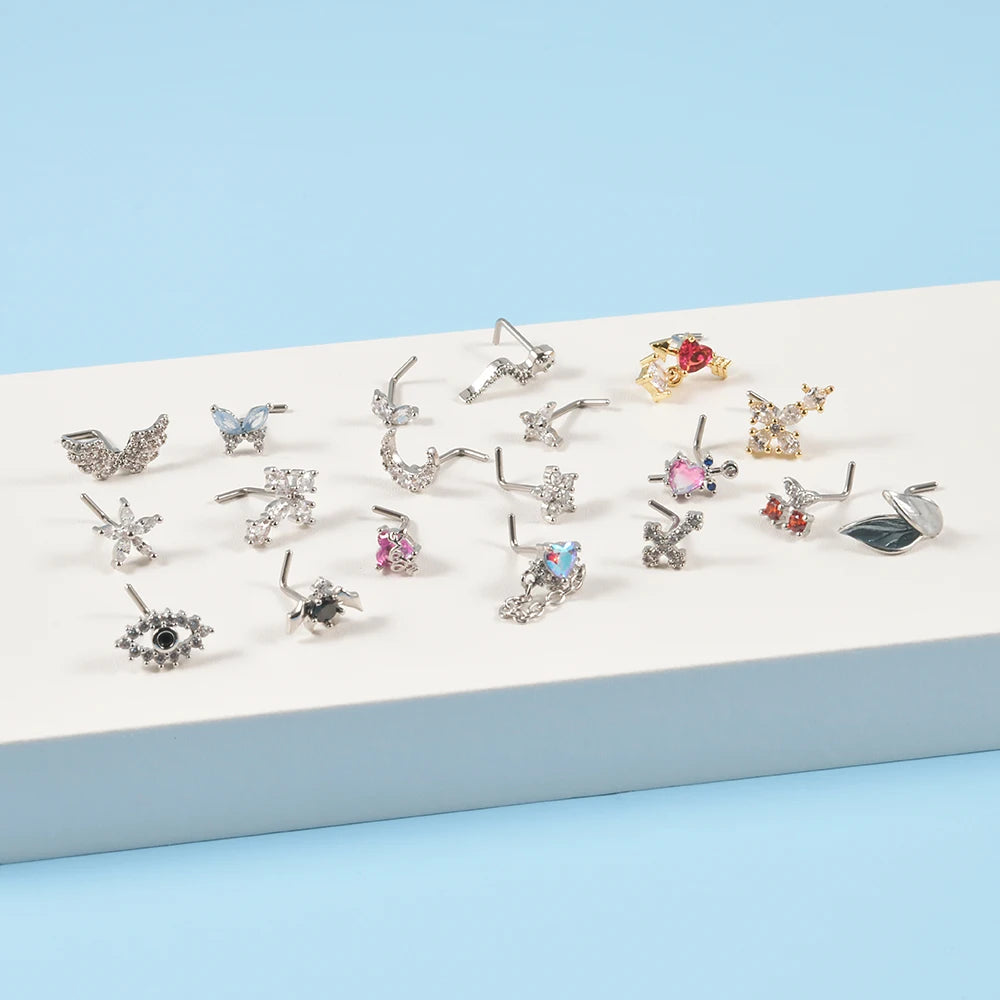 A collection of silver surgical steel demon angel nose studs displayed on a white surface.