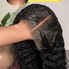 A close-up of a long, dark curly wig being worn on a person's head, demonstrating the seamless glueless application.