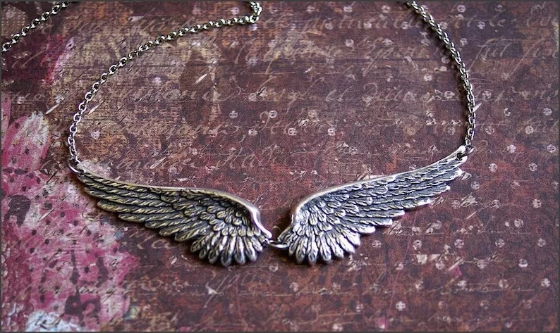 Silver feather angel wings choker necklace resting on a dark, textured surface.