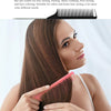 A woman is using a pink pointed tail hair comb and styling brush set on her long brown hair.