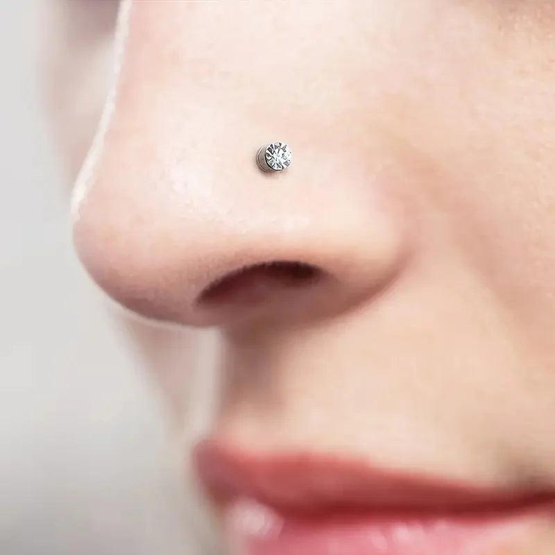 Close-up of a woman's nose featuring a small, round silver stud earring with a cubic zirconia stone.