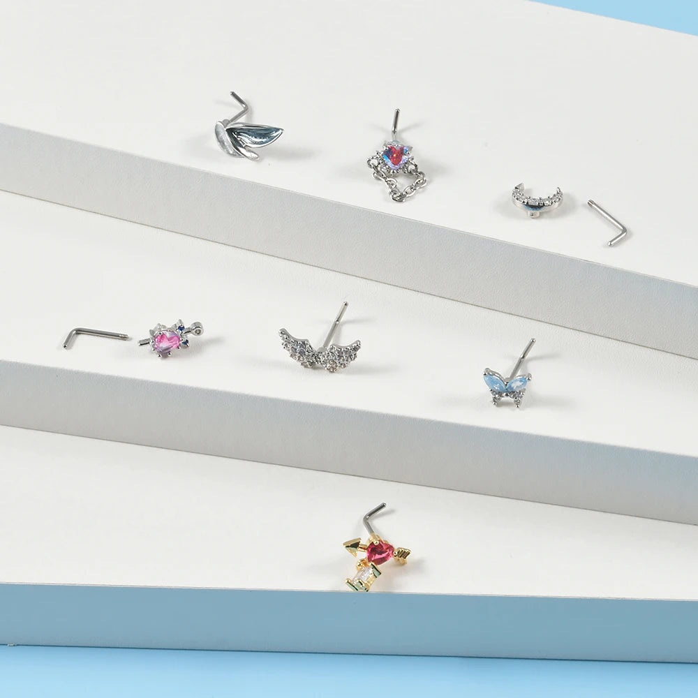 A collection of surgical steel demon angel nose studs and piercings displayed on a white surface.