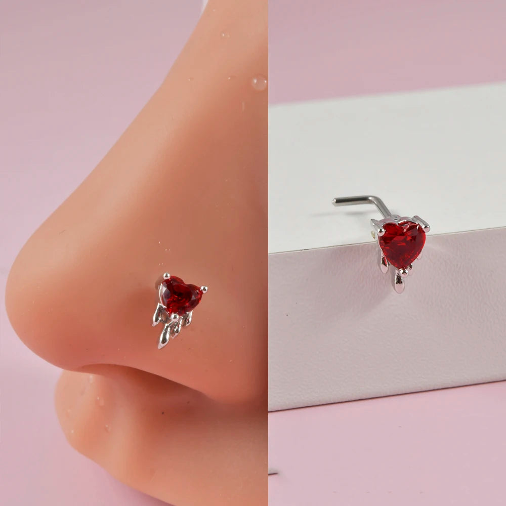 A close-up of a red heart shaped surgical steel demon angel nose stud on a pink nose.