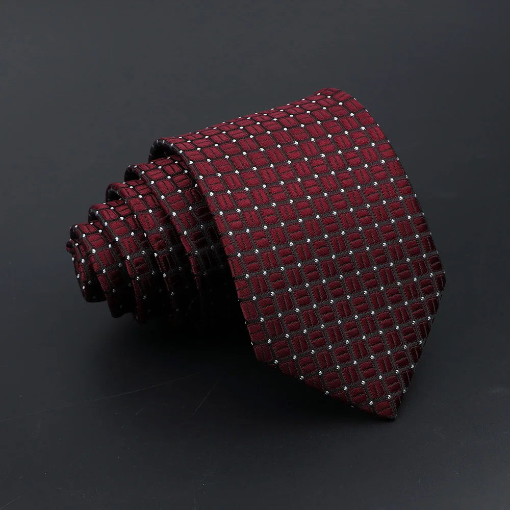 A dark red patterned men's tie rolled up and displayed against a black background.