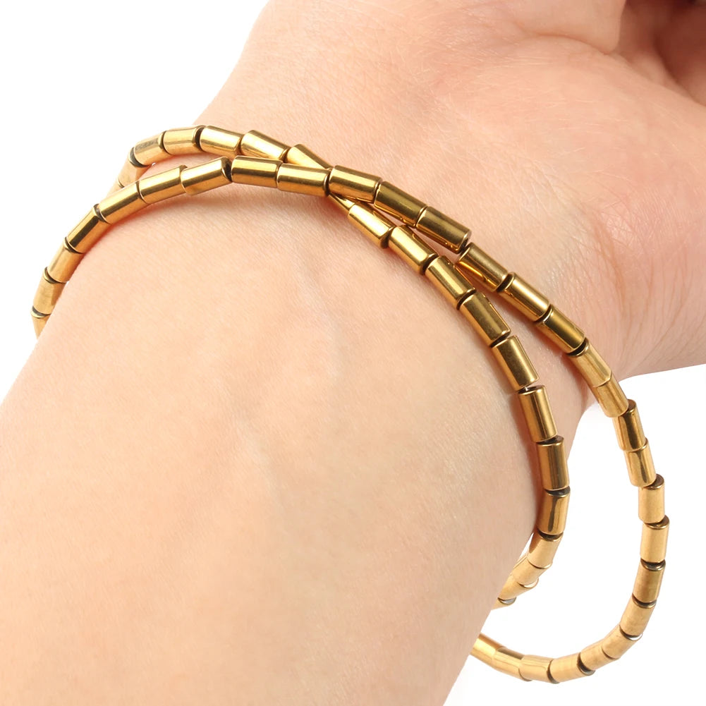 A stack of gold-plated hematite round cube beads for DIY jewelry is shown on a person's wrist.
