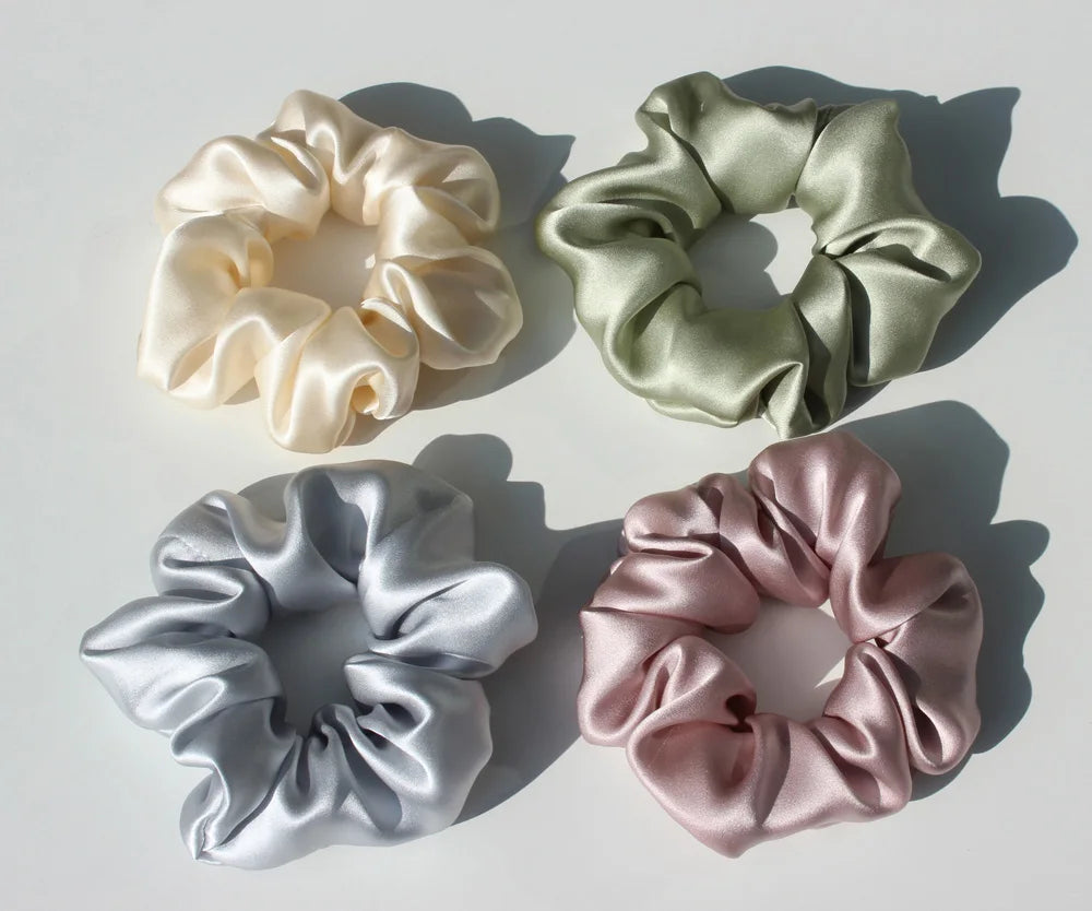 Three silk hair scrunchies in cream, sage green, and dusty rose colors arranged on a white background.