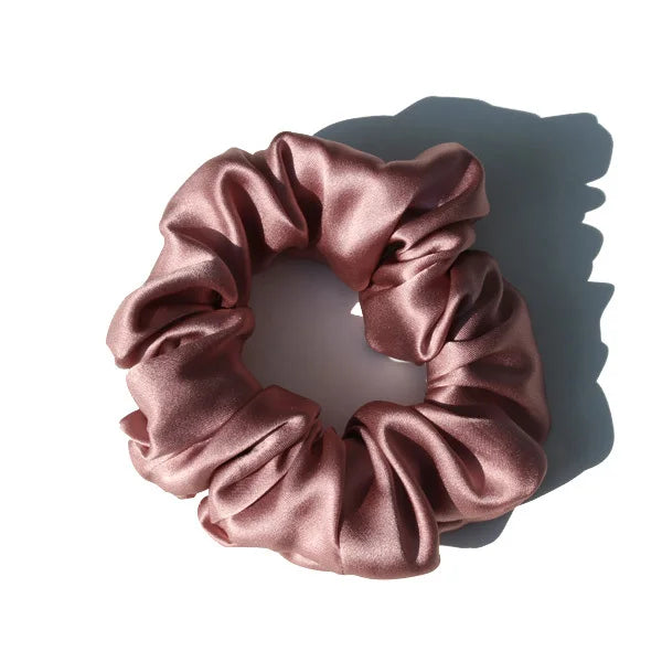 A close-up of a ruched, satin hair scrunchie in a dusty rose color.