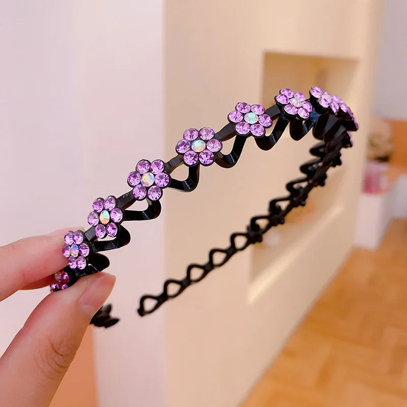 A hand holds a black elastic hair hoop decorated with purple and pink rhinestone flowers.