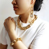 A close-up of a woman wearing a gold boho punk twisted link necklace and bracelet against a white shirt.