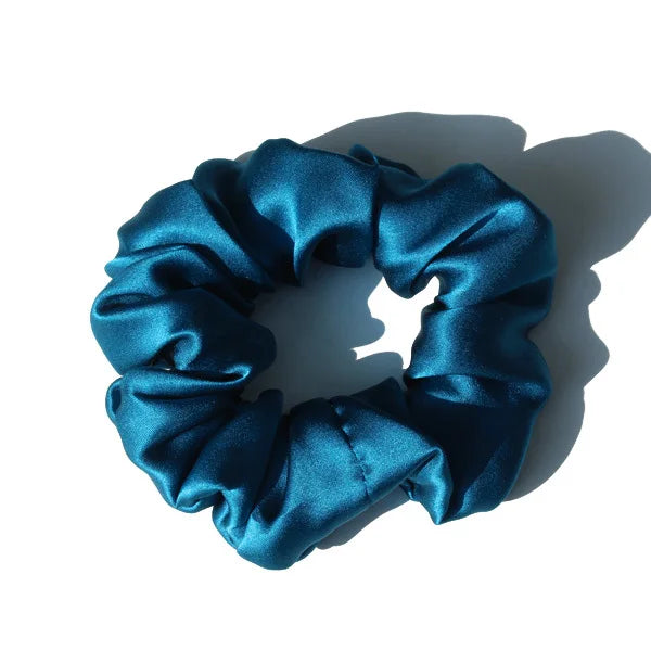 A dark teal silk hair scrunchie tied in a gathered bow, shown against a white background.