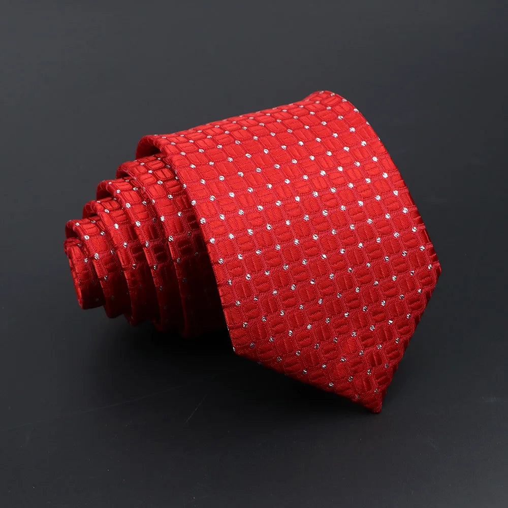 A red silk tie with a repeating pattern of small silver plaid dots, rolled and displayed against a dark background.