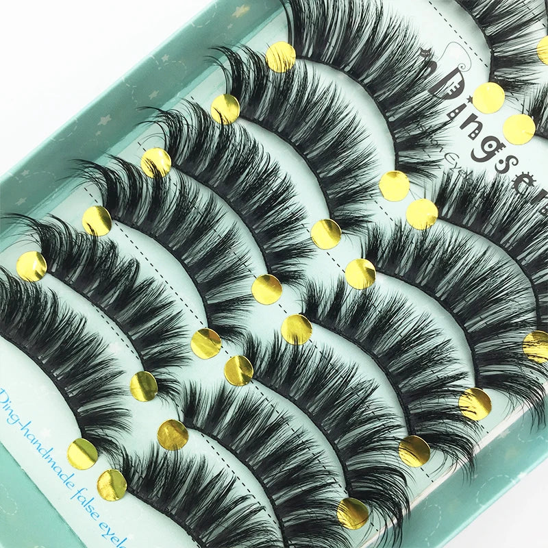 A display of black and gold handmade 3D mink false eyelashes on a light green background.