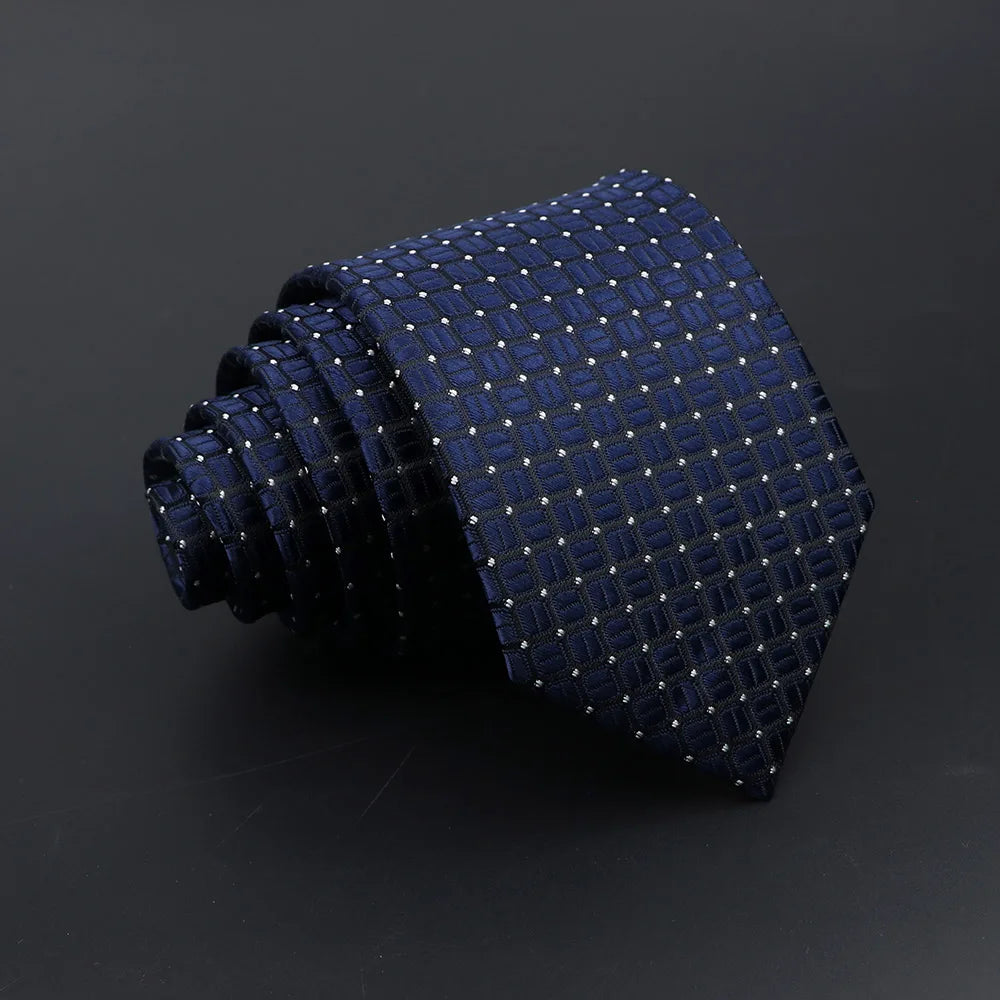 A dark blue patterned men's tie with small gold plaid dots, rolled and displayed on a dark surface.