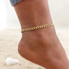 A close-up of a gold stainless steel chain anklet worn on a person's ankle.