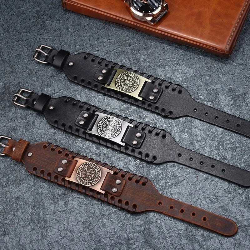 A collection of leather pirate compass bracelets and a brown leather wallet displayed on a gray surface.