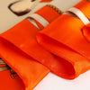 Orange satin silk scarf folded and draped on a white surface.