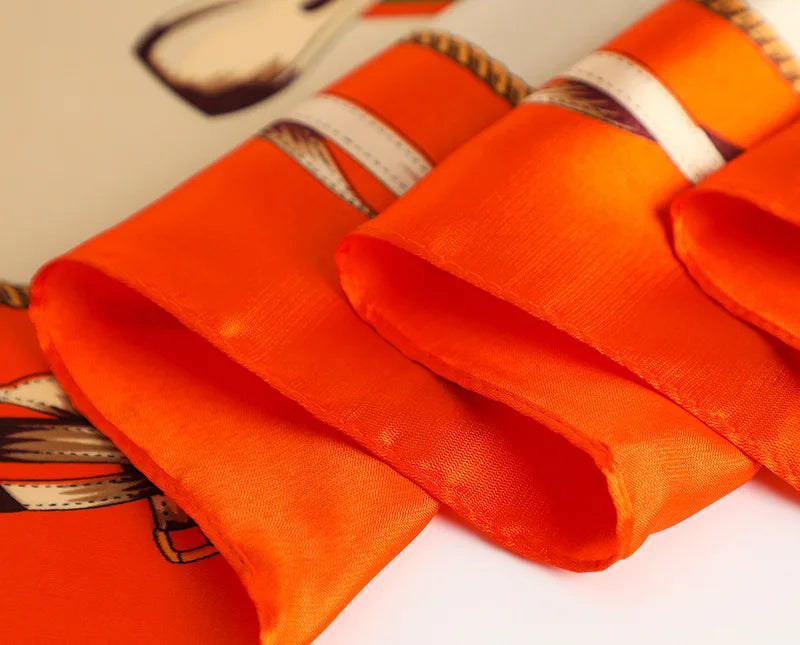 Orange satin silk scarf folded and draped on a white surface.