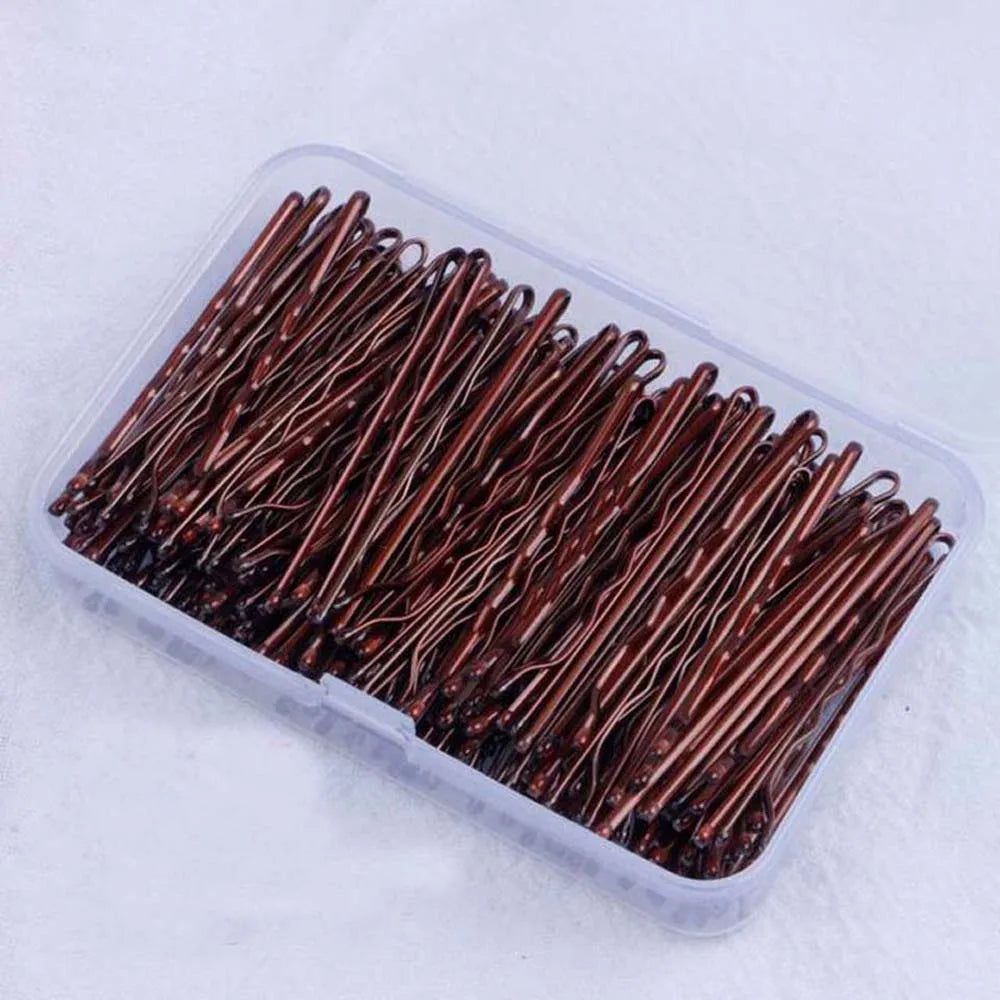 A clear plastic container filled with numerous thin, elegant copper-colored metal hair clips.