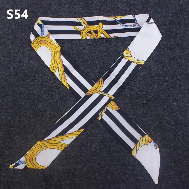 A black and white striped silk headband scarf with gold accents, shaped like an 'X', displayed on a dark gray fabric.