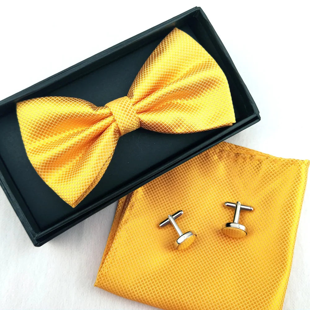 A yellow patterned bow tie and cufflinks are displayed in a black box on a white background.