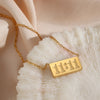 A gold-plated rectangle pendant necklace showing the time 11:11 resting on a white, textured surface.