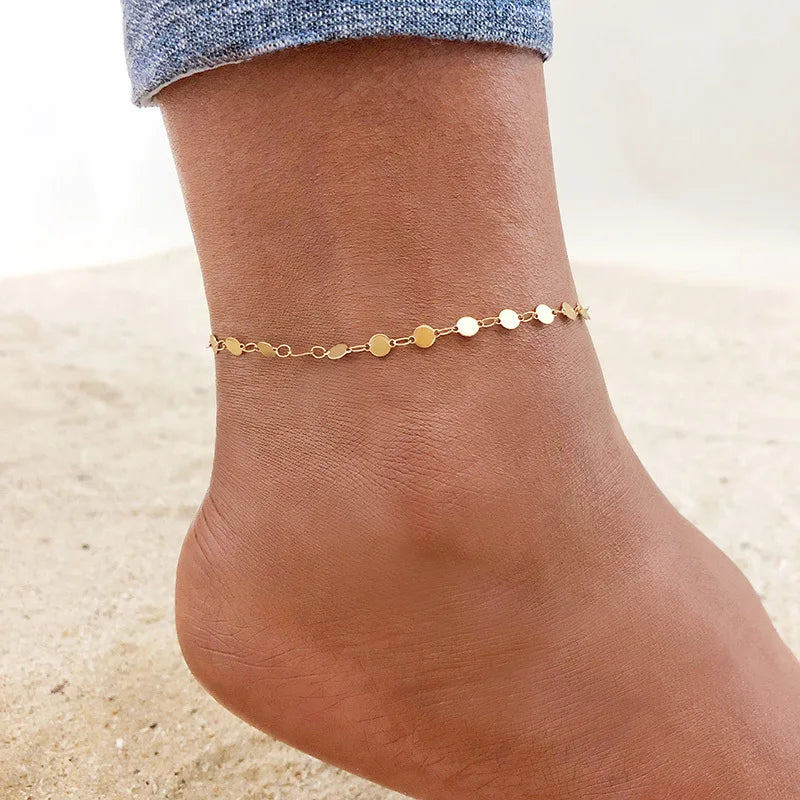 A line of small gold stainless steel anklet charms worn on a person's ankle.