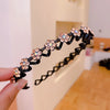 A hand holds a black elastic hair hoop decorated with sparkling pink and orange rhinestones.