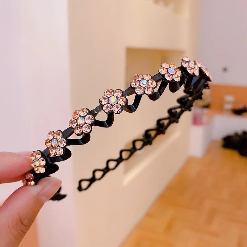 A hand holds a black elastic hair hoop decorated with sparkling pink and orange rhinestones.