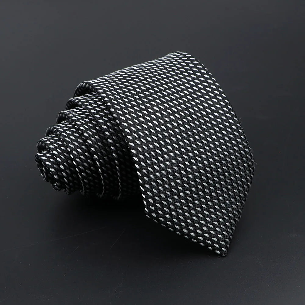 A black classic men's tie with a subtle plaid dot pattern, rolled and displayed on a dark surface.