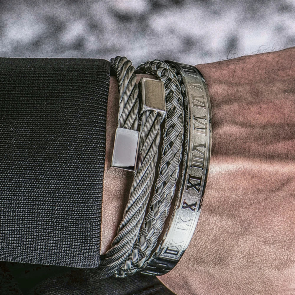 A close-up of a luxury Roman number stainless steel bracelet worn on a wrist against a dark suit sleeve.