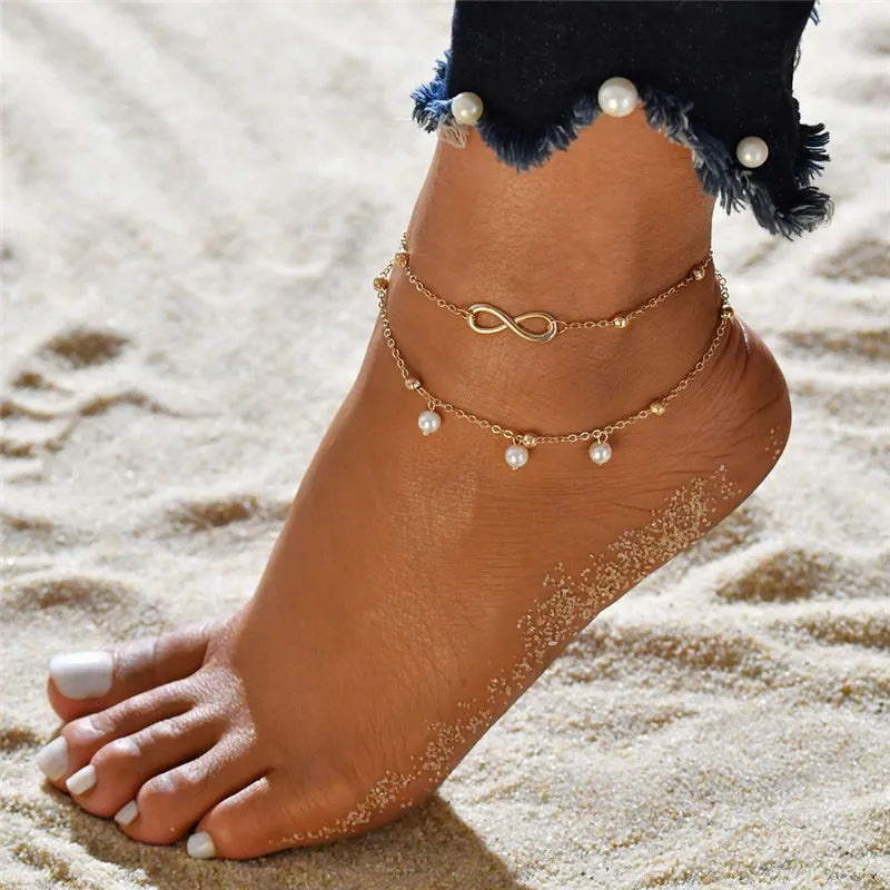 Gold and silver heart chain anklets worn on a foot in the sand