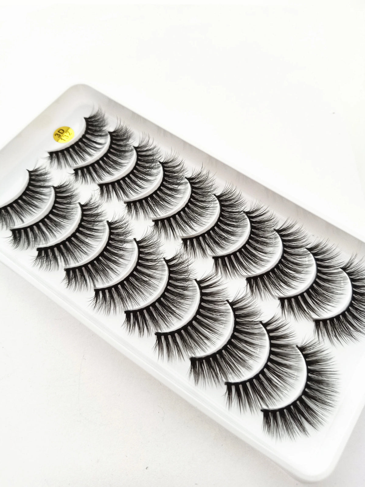 A false eyelash strip featuring a dramatic, layered, curled look displayed on a white plastic tray.