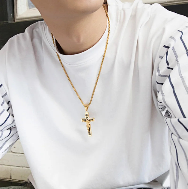 A close-up of a woman wearing a gold retro Christian cross amulet necklace over a white shirt.