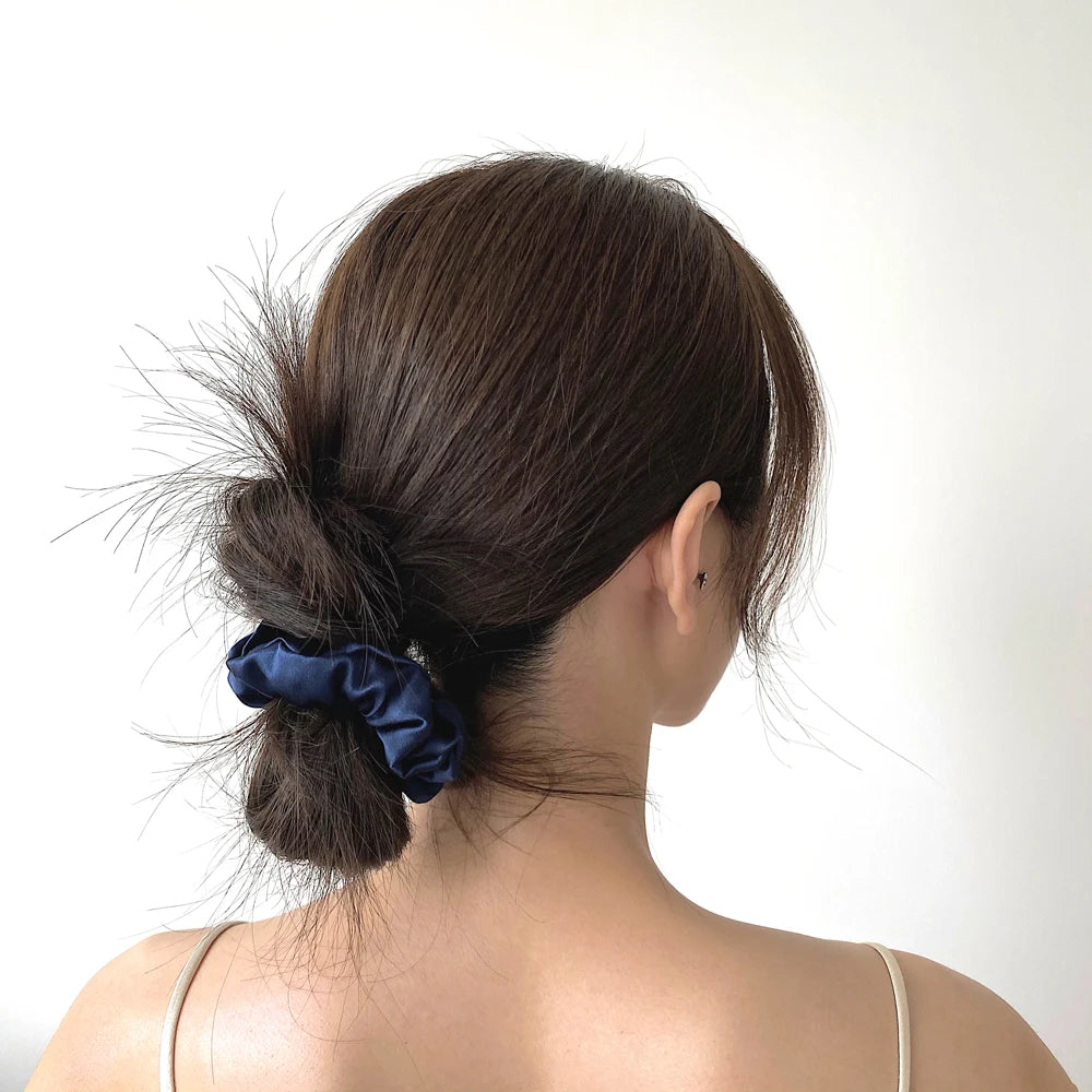 A woman's dark hair is styled in a messy bun secured with a navy blue silk scrunchie.