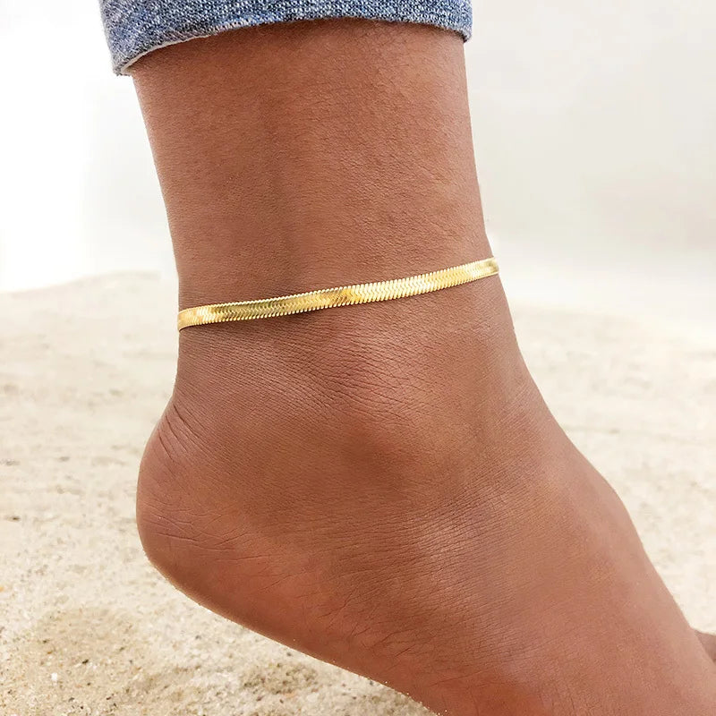A close-up of a woman's ankle wearing a thin gold stainless steel anklet.