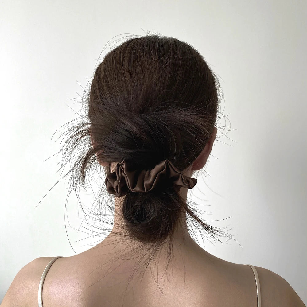 A woman's dark hair is styled in a messy bun with silk scrunchies.