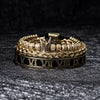 Pulseras de esmalte dorado y negro con números romanos sobre una superficie texturizada oscura.