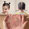 A close-up of colorful disposable hair scrunchies being held in a hand, with a girl's hair styled in ponytails visible in the