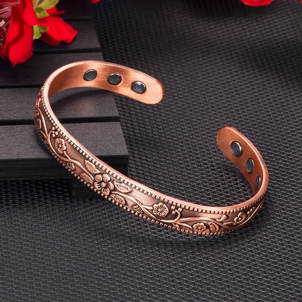 A copper magnetic bangle bracelet featuring intricate plum flower designs on a dark background.
