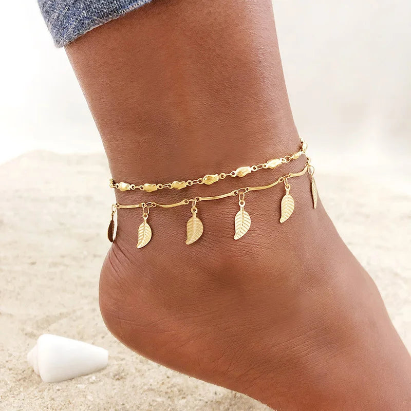 Gold stainless steel anklets with leaf charms worn on a person's ankle.