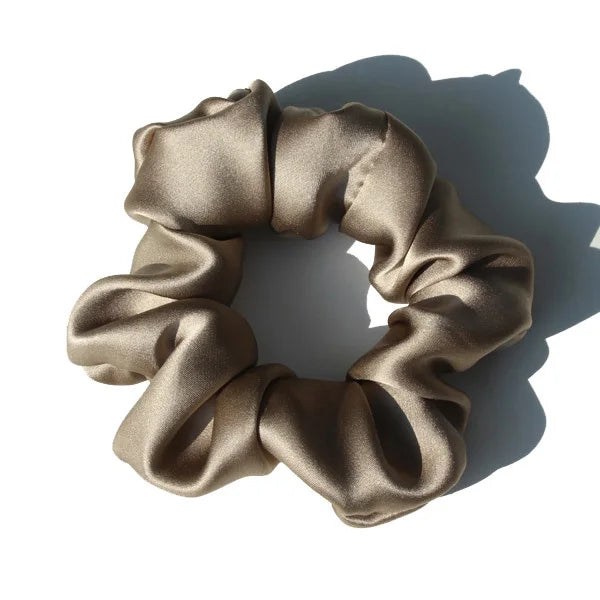 A close-up of a beige silk hair scrunchie tied in a gathered, ruched style.