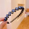 A hand holds a black elastic hair hoop decorated with blue sparkling rhinestones shaped like flowers.