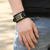 A close-up of a man's wrist wearing a black leather bracelet with a brass pirate compass design.